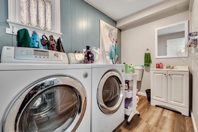 laundry room featuring wooden walls, a sink, light wood-style flooring, and washing machine and clothes dryer