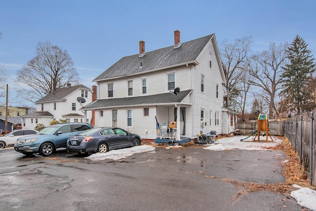 rear view of house featuring a shingled roof, a chimney, a playground, and fence