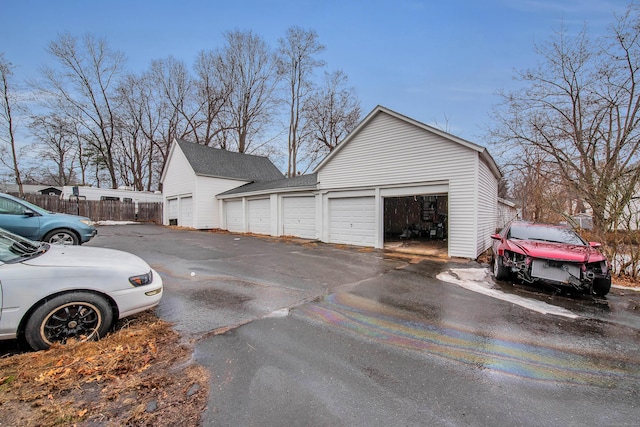 view of home's exterior featuring a shingled roof, fence, and community garages