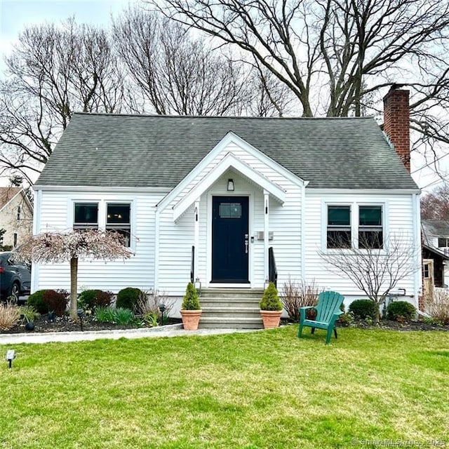 view of front of property featuring entry steps, a chimney, a front lawn, and roof with shingles