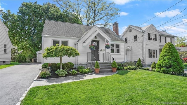 view of front of property featuring a shingled roof, a chimney, and a front lawn