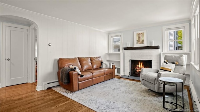 living area with arched walkways, a fireplace, wood finished floors, ornamental molding, and baseboard heating