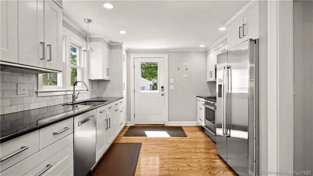 kitchen with tasteful backsplash, appliances with stainless steel finishes, ornamental molding, white cabinetry, and a sink