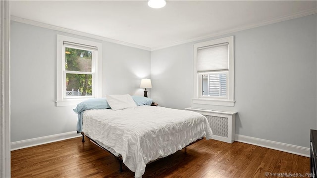 bedroom with crown molding, radiator heating unit, wood finished floors, and baseboards