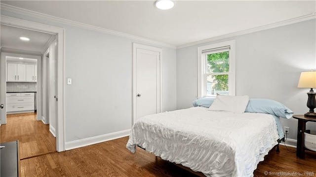 bedroom with baseboards, a closet, wood finished floors, and crown molding