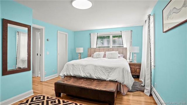 bedroom with baseboard heating, light wood-style flooring, and baseboards