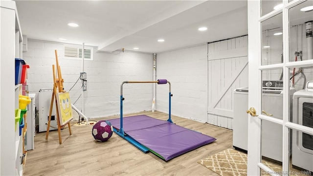 workout area featuring concrete block wall, wood finished floors, recessed lighting, and separate washer and dryer