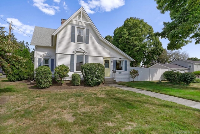 view of front facade featuring entry steps, a shingled roof, a chimney, fence, and a front lawn