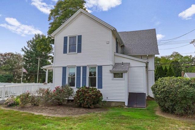 rear view of property featuring roof with shingles, a lawn, and fence