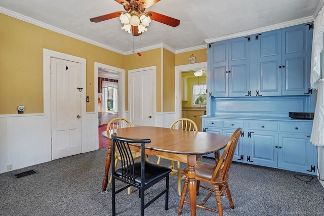 dining room with visible vents, a ceiling fan, ornamental molding, wainscoting, and dark carpet