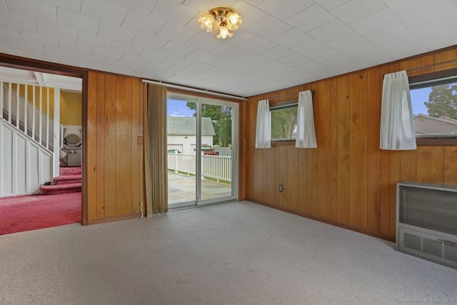 unfurnished living room with carpet floors, heating unit, wooden walls, and stairway