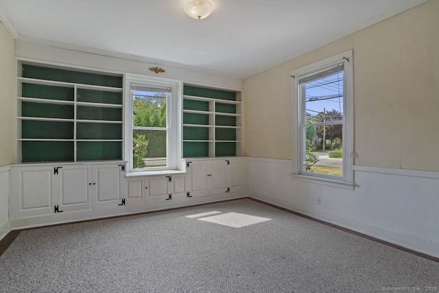 unfurnished room with built in shelves, wainscoting, carpet flooring, and baseboards