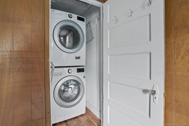 clothes washing area featuring stacked washing maching and dryer, laundry area, and wood finished floors