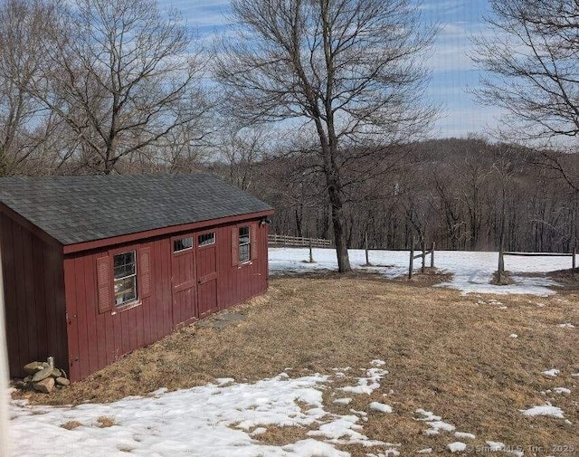 yard covered in snow featuring an outbuilding, a shed, and a wooded view