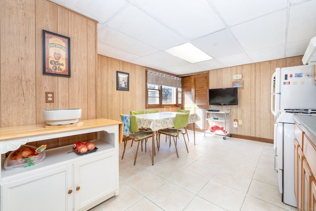 dining area featuring light tile patterned floors, wood walls, and a paneled ceiling