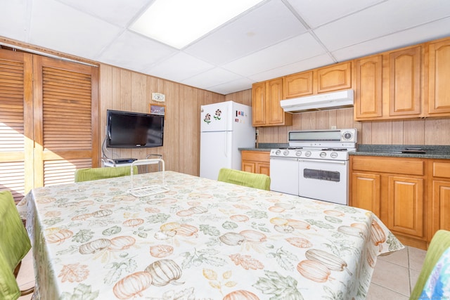 kitchen with dark countertops, wooden walls, under cabinet range hood, white appliances, and a paneled ceiling