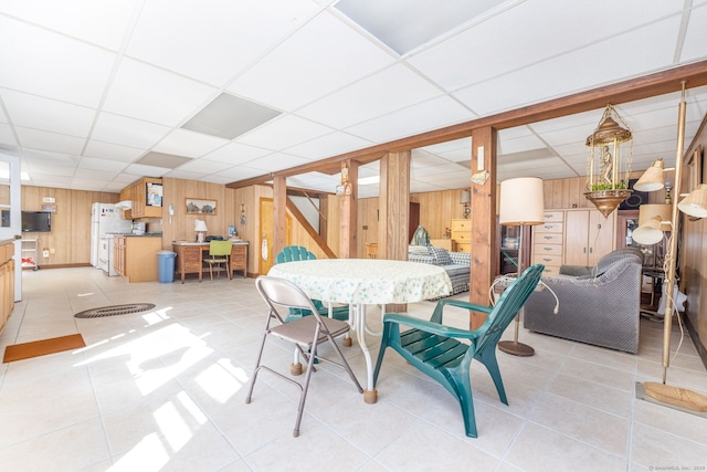 dining room with light tile patterned floors, wooden walls, and a paneled ceiling