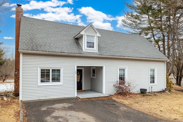 view of front of home featuring a patio, aphalt driveway, roof with shingles, and a chimney