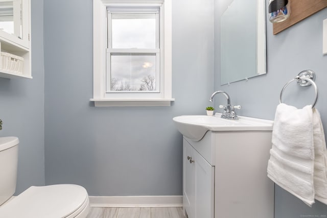 half bath with toilet, baseboards, and vanity