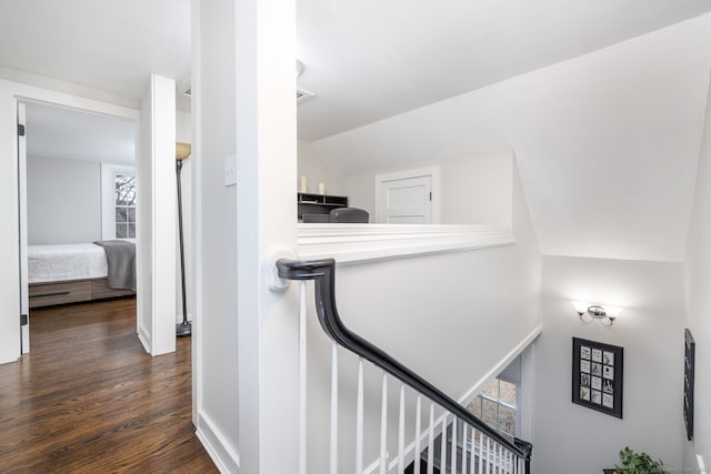 corridor with vaulted ceiling, dark wood finished floors, and an upstairs landing