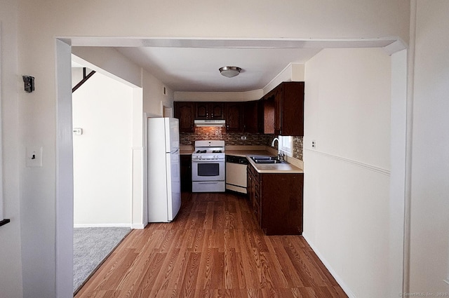 kitchen featuring white appliances, wood finished floors, dark brown cabinets, under cabinet range hood, and a sink