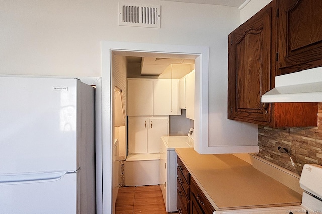 kitchen with washer / dryer, visible vents, freestanding refrigerator, light countertops, and under cabinet range hood