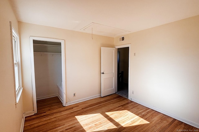 unfurnished bedroom with a closet, visible vents, attic access, light wood-style floors, and baseboards