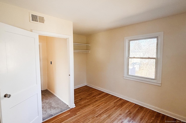 unfurnished bedroom with baseboards, wood-type flooring, visible vents, and a closet