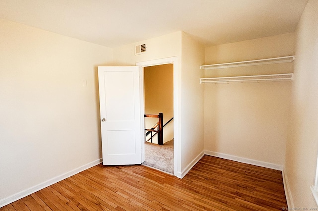 unfurnished bedroom with a closet, wood-type flooring, visible vents, and baseboards