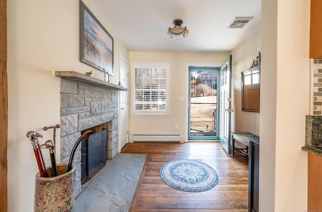 doorway featuring baseboard heating, a stone fireplace, visible vents, and wood finished floors