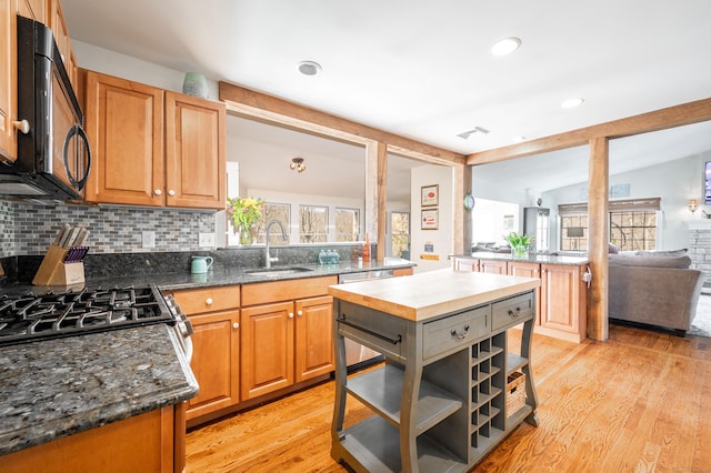 kitchen featuring light wood finished floors, vaulted ceiling with beams, appliances with stainless steel finishes, and a sink