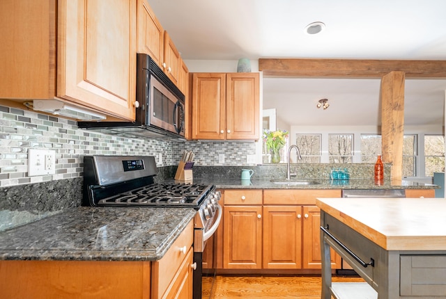 kitchen featuring light wood-type flooring, a sink, stainless steel appliances, dark stone counters, and decorative backsplash