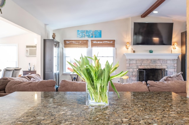 living room featuring a wealth of natural light, a stone fireplace, vaulted ceiling with beams, and a wall mounted AC