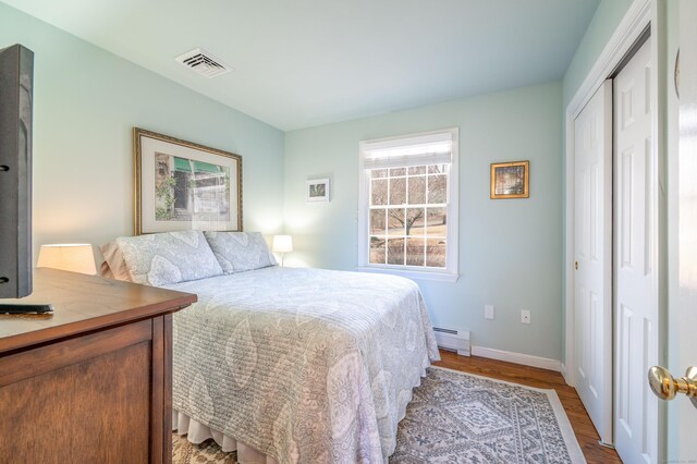 bedroom featuring visible vents, a baseboard heating unit, wood finished floors, a closet, and baseboards