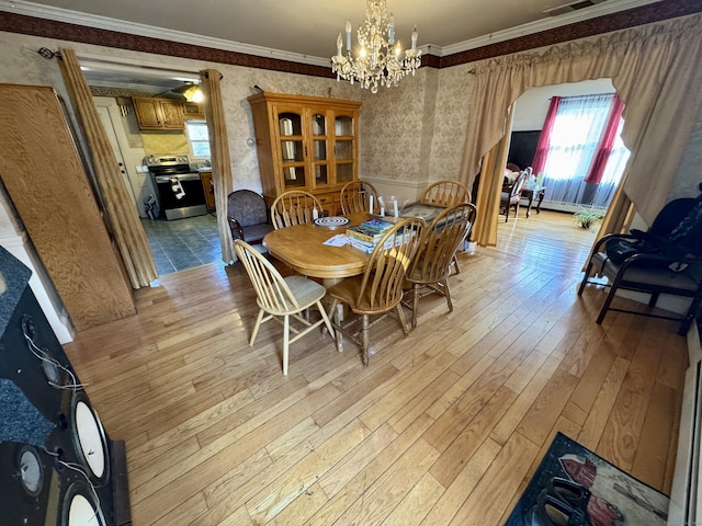 dining space with ornamental molding, light wood-type flooring, a notable chandelier, and wallpapered walls