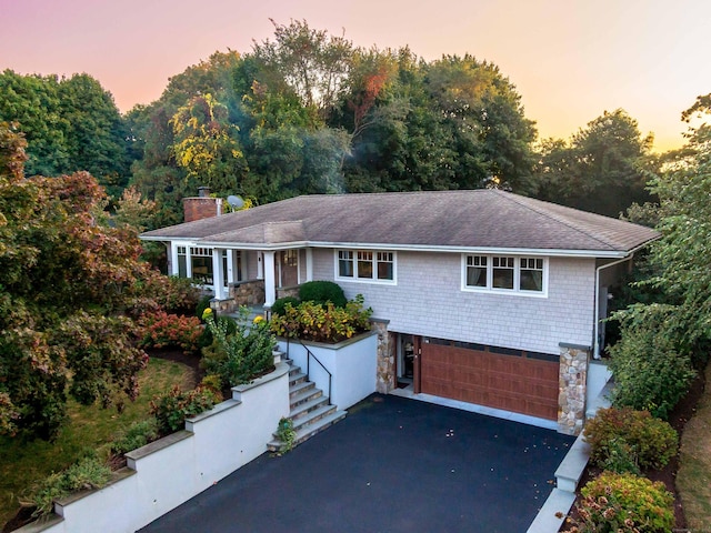 view of front facade featuring a chimney, a porch, an attached garage, driveway, and stairs