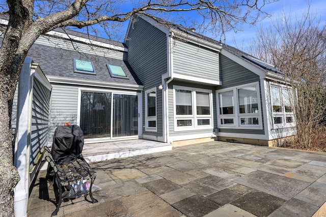 rear view of house with roof with shingles and a patio area