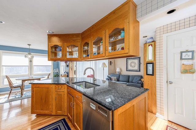 kitchen with stainless steel dishwasher, brown cabinetry, glass insert cabinets, a sink, and dark stone countertops