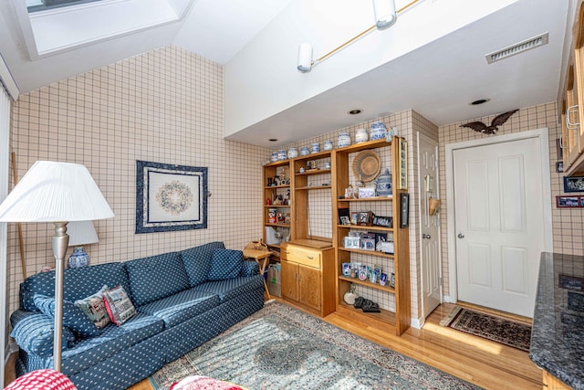 living room with lofted ceiling, visible vents, tile walls, and wood finished floors