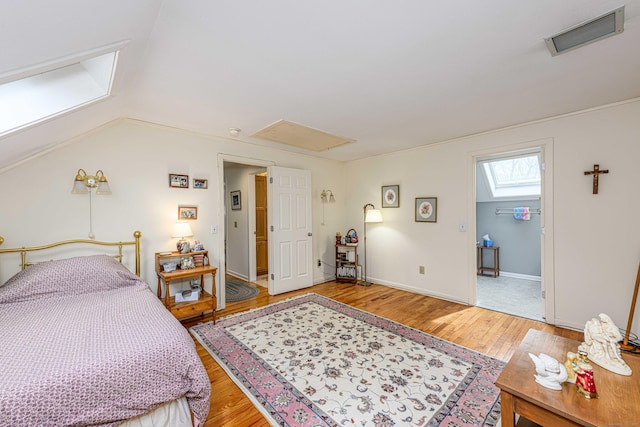 bedroom featuring light wood-style flooring, lofted ceiling with skylight, visible vents, and baseboards