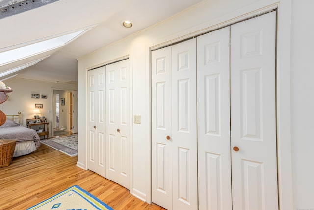 bedroom with a skylight, ornamental molding, light wood finished floors, and multiple closets