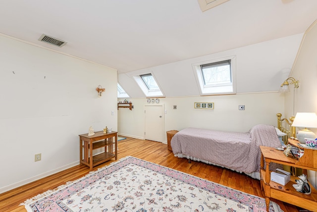 bedroom featuring baseboards, vaulted ceiling with skylight, visible vents, and wood finished floors