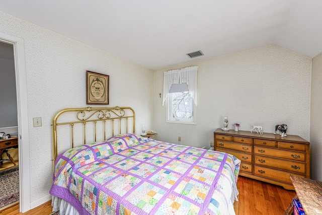 bedroom with visible vents, vaulted ceiling, and wood finished floors