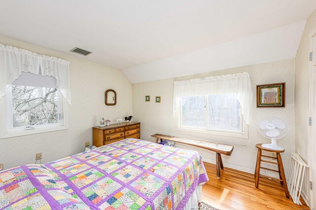 bedroom with visible vents, vaulted ceiling, light wood finished floors, and multiple windows