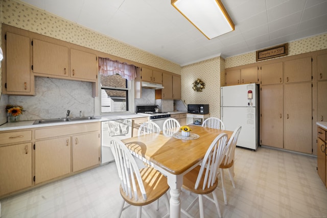 kitchen with white appliances, wallpapered walls, light floors, under cabinet range hood, and a sink