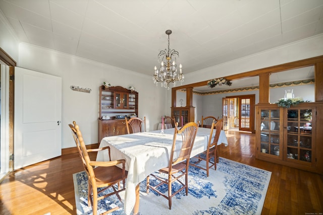 dining room featuring hardwood / wood-style flooring, a notable chandelier, baseboards, decorative columns, and crown molding