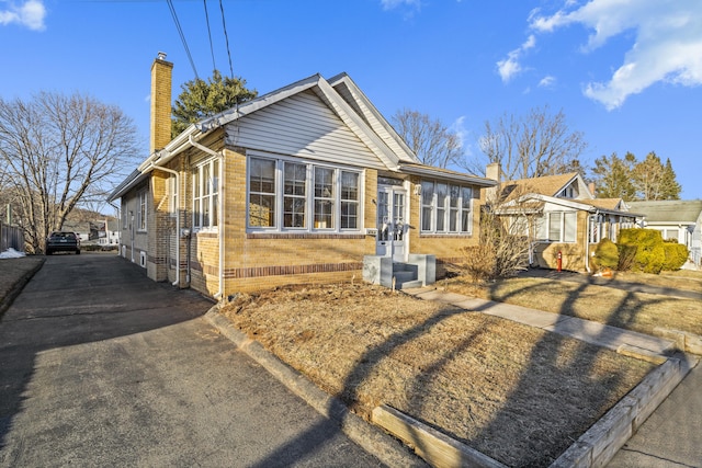 view of front facade featuring driveway, a chimney, and brick siding