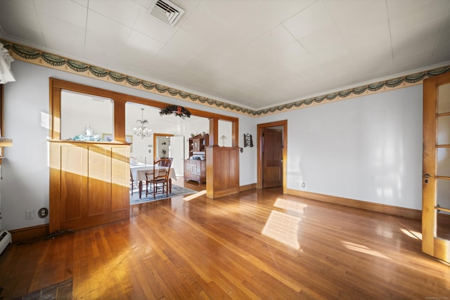 unfurnished room with a notable chandelier, visible vents, a baseboard heating unit, baseboards, and hardwood / wood-style flooring