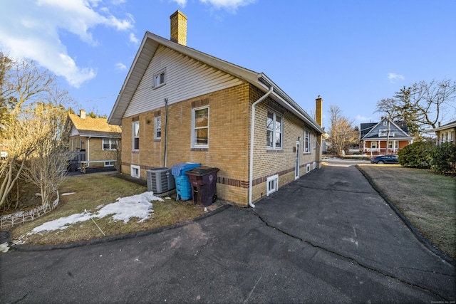 view of home's exterior featuring brick siding, a chimney, and cooling unit