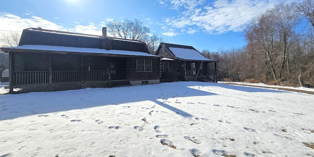 snow covered rear of property with covered porch and log siding